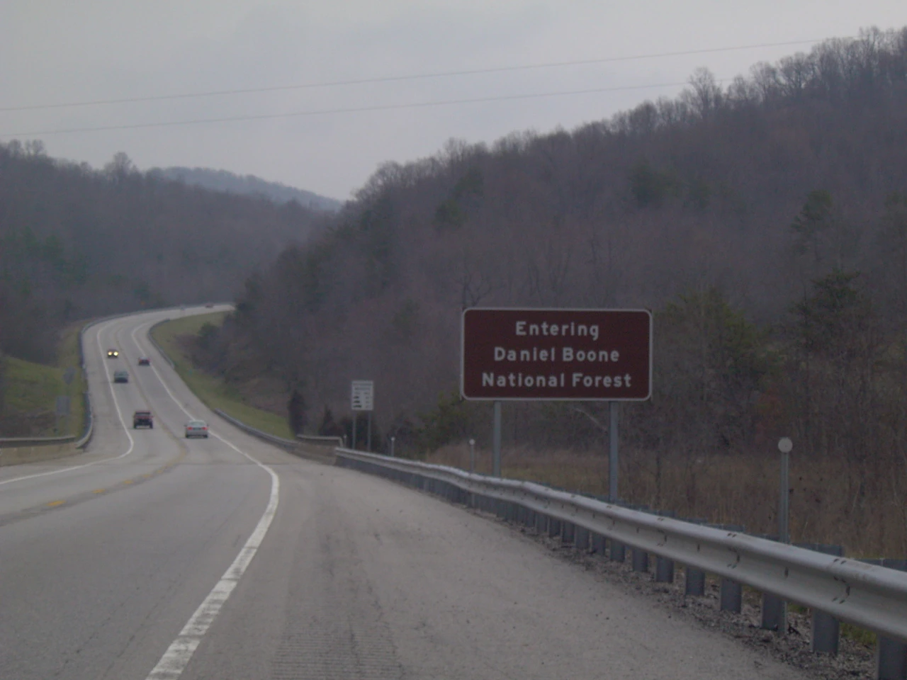 A road curves between wooded hills beside a sign for Daniel Boone National Forest.